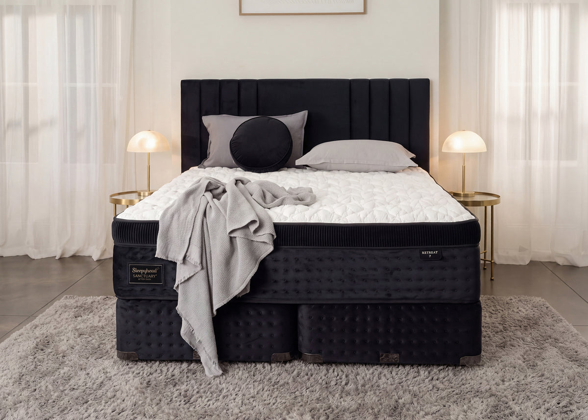 A luxury mattress set in a modern bedroom, featuring a black tufted box spring and matching headboard, a white mattress topper, gray pillows, and a draped gray throw blanket.